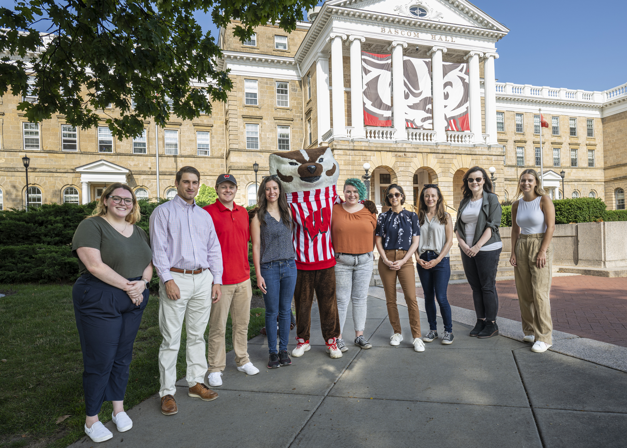 A group of eight people poses with Bucky Badger, the University of Wisconsin–Madison mascot, outdoors in front of Bascom Hall.