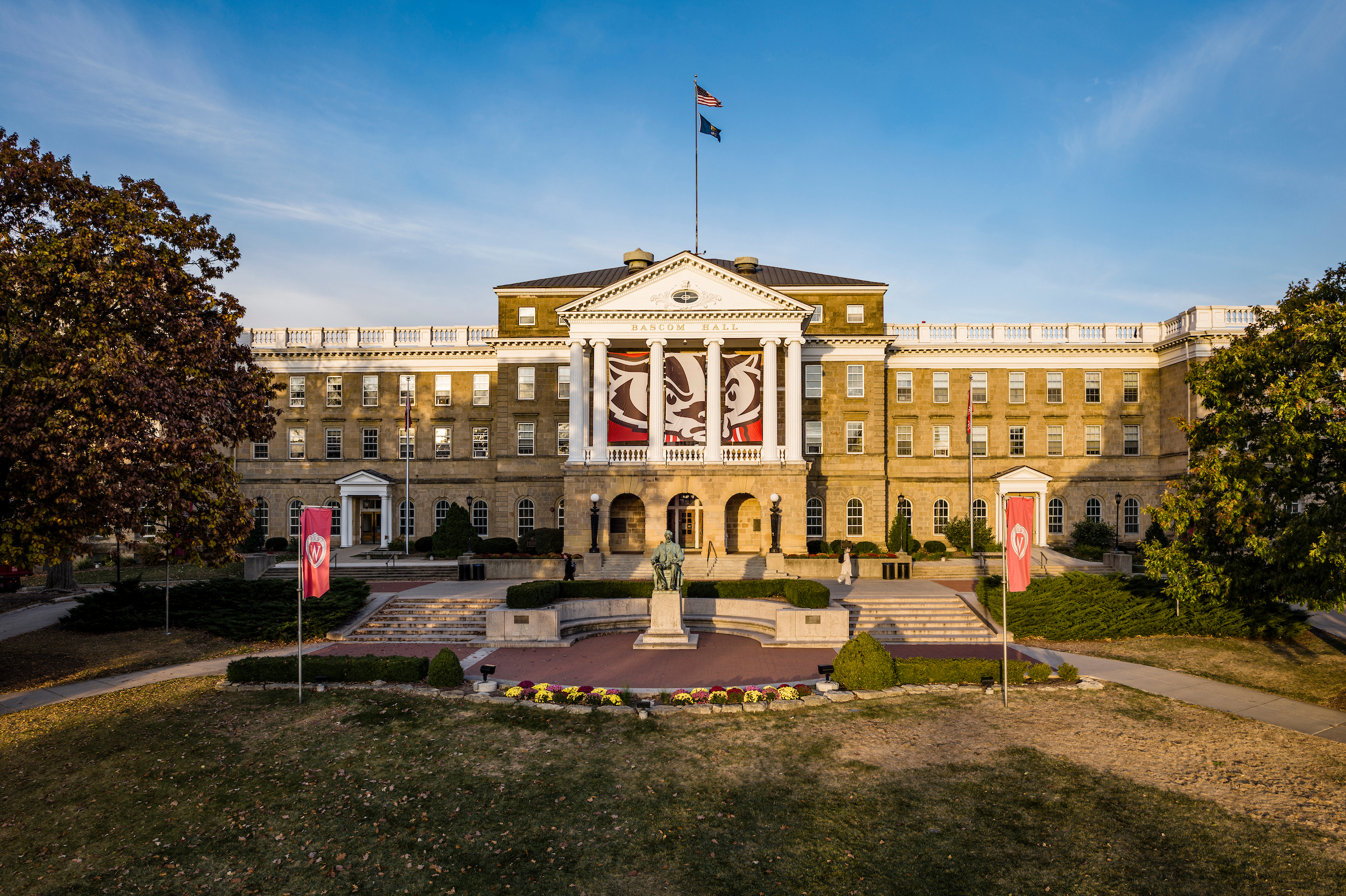 Exterior view of the UW–Madison's Bascom Hall at sunrise with banners, a statue, and a well-manicured lawn.